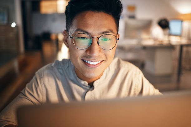 Laptop, information technology and business man in night office for web design, software development or IT code analysis. Asian man glasses with screen reflection working at an online global company