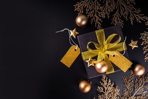 Black gift box with golden ribbon bow on black background.