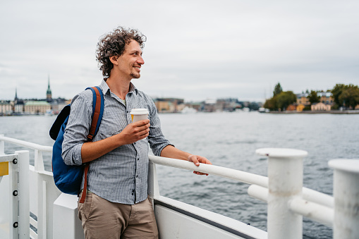 Handsome young man drinking coffee on the tour boat in Stockholm, Sweden.