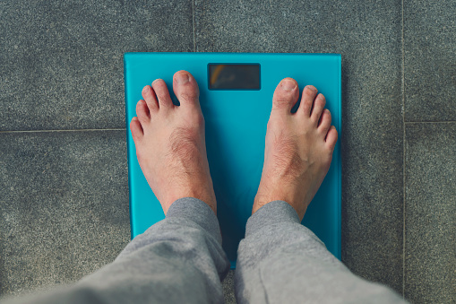 Man standing on weight scale. Male feet on glass scales, men's diet, body weight, close up, man stepping up on scales, side view