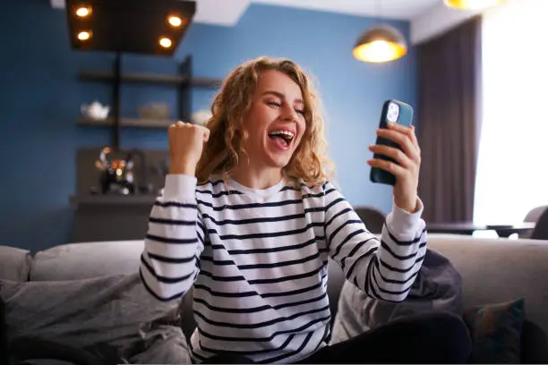 Photo of Female rejoice, celebrate a prize, big lottery win, auction victory, profitable bet on crypto stock market. Woman checks e-mail, news about success on smartphone or cellphone.