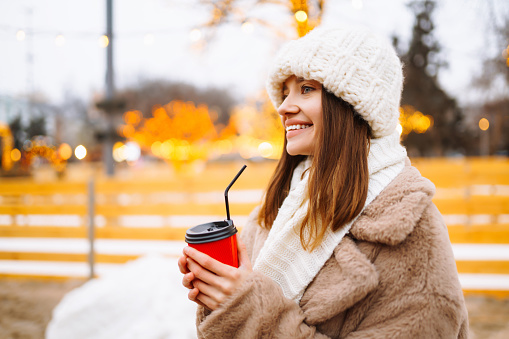 Happy woman with disposable paper coffee cup in winter over outdoor ice skating rink on background. Christmas, hot drinks and holidays concept.