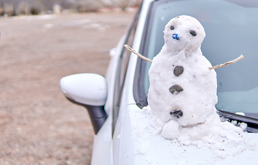 Snowman sitting outside on top of white car parked on the side of the road in Mendoza, Argentina.