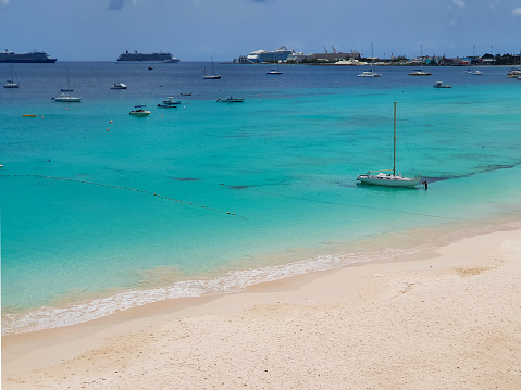 beautiful tropical beach with blue turquoise water in the ocean, Barbados. View on port, ships, vessels, cruises and fishing boats in harbor. Wave meet sand