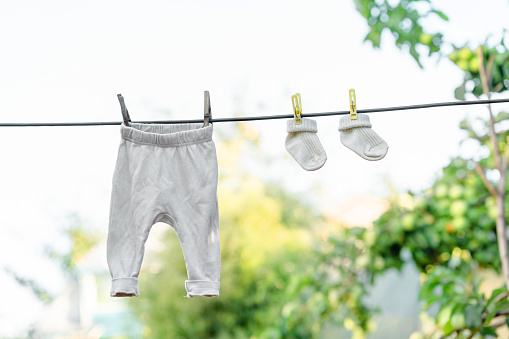 Baby clothes socks and pants for a newborn are hung on a rope with clothespins on a background of blue sky and leaves