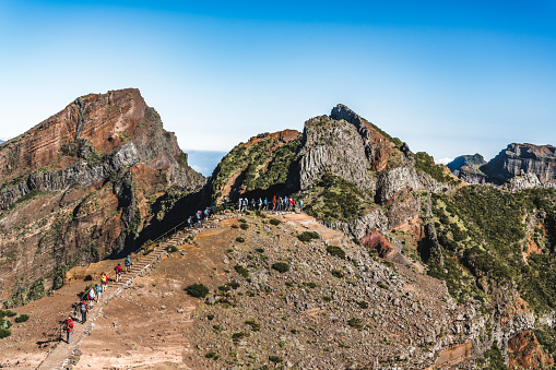 A queue of tourists seen from afar on a mountain trail on a beautiful sunny day in Madeira.
