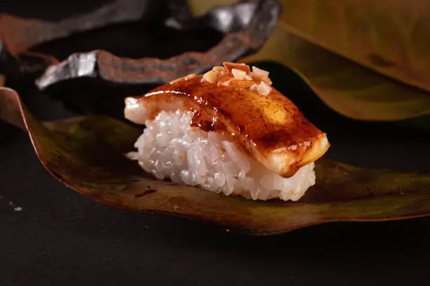 Flamed nigiri and Japanese sushi rice, delicious Japanese food with black background and decorated with leaves and soy sauce, for oriental and Asian food restaurant.