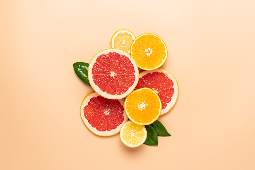 Composition of neatly arranged ripe grapefruit, orange, lemon, green leaves on beige background