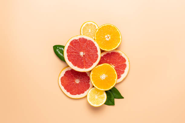 Slices of citrus fruits laid out on a beige background Composition of neatly arranged ripe grapefruit, orange, lemon, green leaves on beige background citrus fruit stock pictures, royalty-free photos & images
