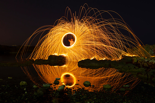 Iron wool circle drawing fireworks, steel wool spining makes reflection on the water.