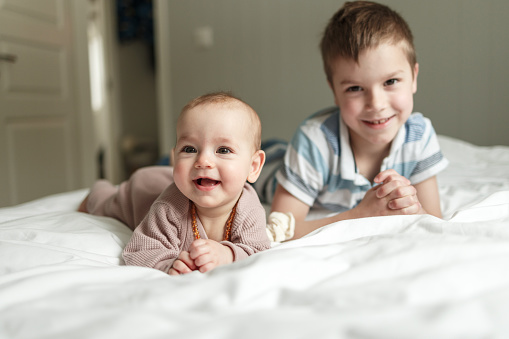 Portrait of a happy brother and baby sister lying on the bed at home