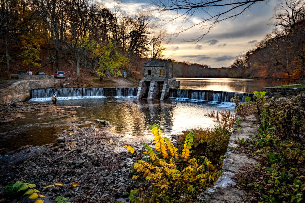 Morristown, NJ - USA - Nov 5, 2022 An autumnal horizontal wide angle view of New Jersey's historic stone Speedwell Dam during sunset. Fly fisherman in the foreground and people hiking in the distance. morristown, nj - ee.uu. - nov 5, 2022 una vista otoñal horizontal de gran angular de la histórica presa de piedra speedwell de nueva jersey durante la puesta de sol. pescadores con mosca en primer plano y personas caminando en la distancia.