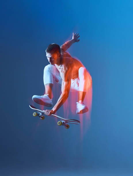 un jeune skateur cool saute sur du skateboard en studio sur fond bleu. skateboarder attrapant une planche en l’air. - sporting position vitality blurred motion strength photos et images de collection