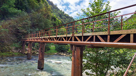 Fast mountain river in Georgia. Rusty iron pedestrian bridge. Caucasus.