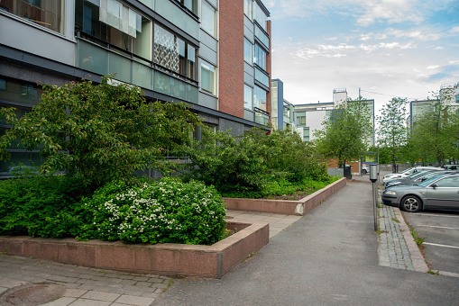 06-22-2022 Helsinki , Finland.   Garden next to a residential building (5 floors) and a garden - green grass and trees, bounded by stone fences and cars in parking lots