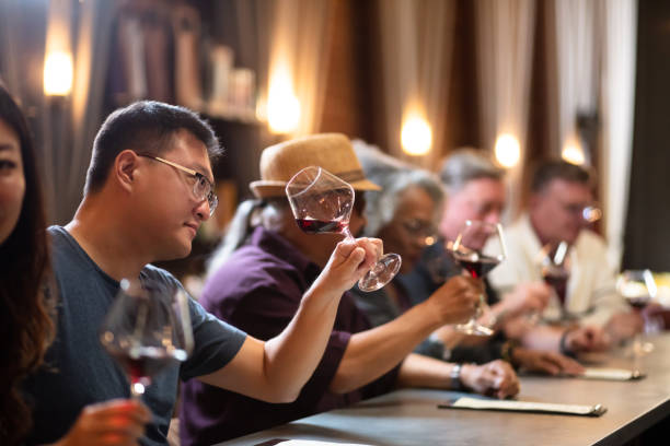 Man Inspecting Wine in Glass at Crowded Bar A diverse group of people sitting at the bar in an elegant wine tasting lounge in Northern California, drinking and chatting. wine bar counter stock pictures, royalty-free photos & images
