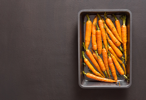 Roasted honey glazed carrots on baking tray over dark stone background with free text space. Top view, flat lay