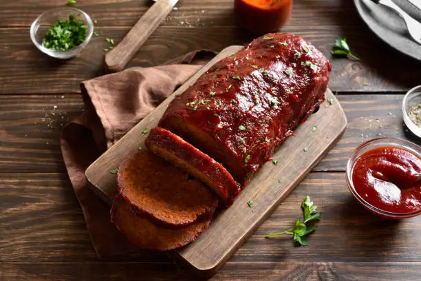 Meatloaf with glaze on cutting board over wooden background. Close up view