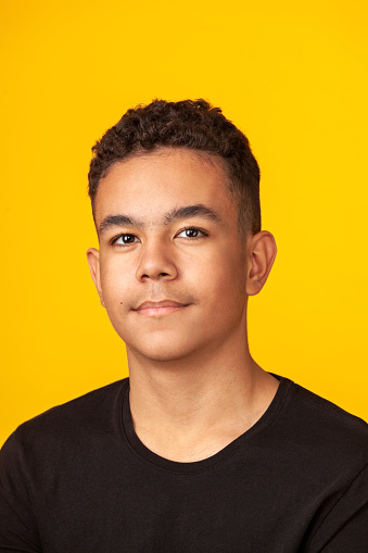 Close-up studio portrait of a 13 year old teenager boy in a black t-shirt against a yellow background