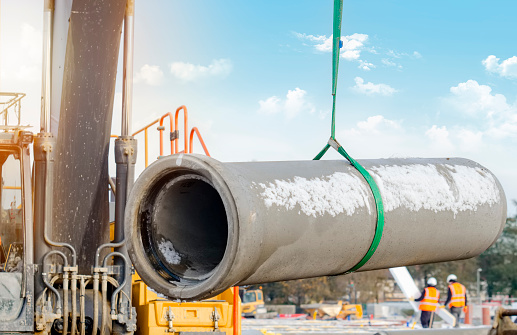 Concrete drainage pipe lifted by excavator during deep drainage works on construction site