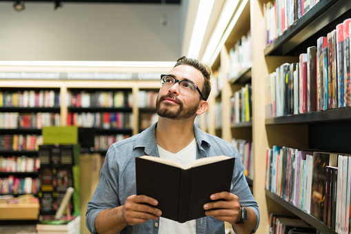 Thoughtful reflexive man thinking and using his imagination while reading a novel at the book shop