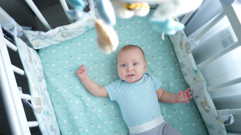 Baby girl looks at musical mobile with plush toys and smiles