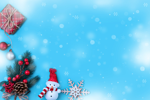 Blue Christmas background with snowflakes, gift box, fir tree branch and pine cones, holiday decorations and snowman. Winter holidays design with copy space for text. Top view.