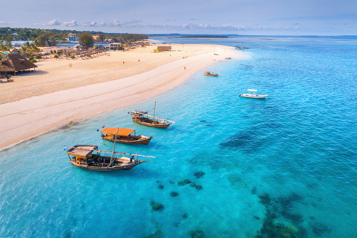 Aerial view of the fishing boats on tropical sea coast with sandy beach at sunset. Summer holiday on Indian Ocean, Zanzibar, Africa. Landscape with boat, palm trees, transparent blue water. Top view