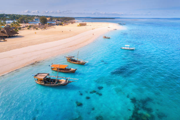 Aerial view of the fishing boats on tropical sea coast with sandy beach at sunset. Summer holiday on Indian Ocean, Zanzibar, Africa. Landscape with boat, palm trees, transparent blue water. Top view stock photo