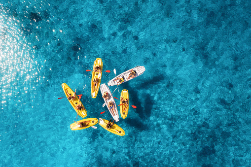 Aerial view of yellow kayaks in blue sea at sunset in summer. People on floating canoes in clear azure water. Sardinia island, Italy. Tropical landscape. Sup boards. Active travel. Top view from drone