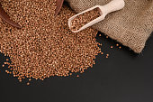 Buckwheat seeds in a wooden spoon, top view on a black table. Healthy food. Selective focus.