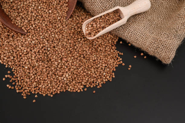 sementes de trigo sarraceno em uma colher de pau, vista superior em uma mesa preta. alimentação saudável. foco seletivo. - buckwheat groats - fotografias e filmes do acervo