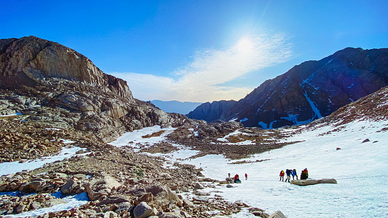 Mount Whitney, California, USA – Apr 30, 2022: Nature beauty on the way to Mt Whitney summit via snow chute. There are anonymous people that can be seen unclear in the distance. Picture take in the middle of the snow hiking trail at the sunrise. Mt Whitney is the highest mountain in the 48 contiguous states of USA.