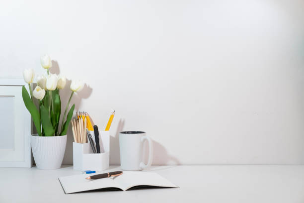 istock Feminine workspace with flower pot, coffee cup, picture frame and stationery on white table. 1440628030