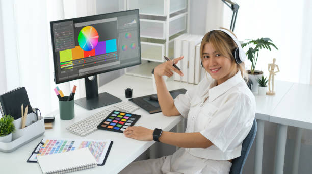 istock Smiling asian female graphic designer wearing headphone sitting front of computer sat her home office. 1440632593