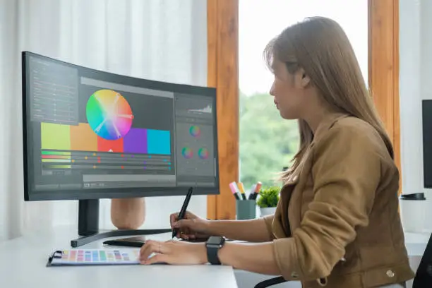 Photo of Side view of young woman sitting at graphic studio and choosing color for creative project on computer screen.