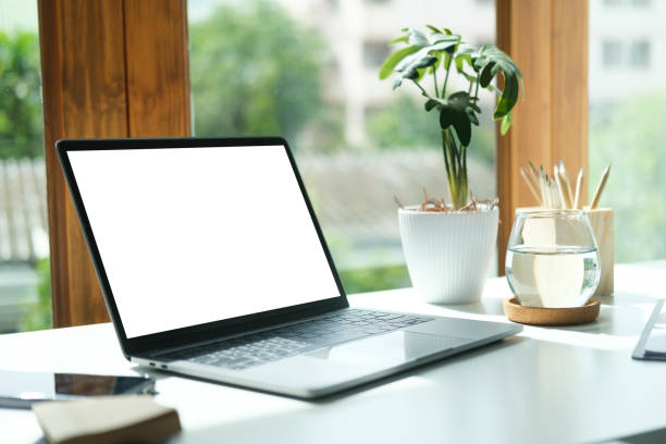 istock Laptop computer with empty screen, stationery and potted plant on white table in bright office. 1440633438