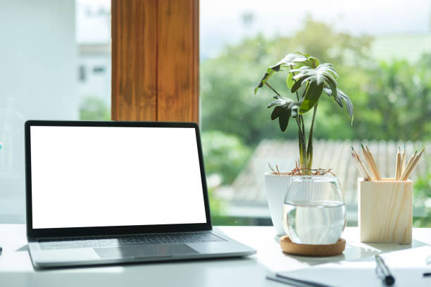 istock Laptop computer with empty screen, stationery and potted plant on white table in bright office. 1440633467
