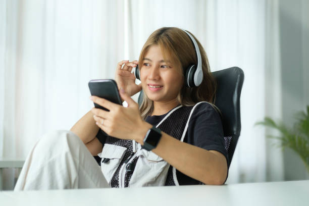 istock Pleased young woman with wireless headphone using mobile phone in home office. 1440634126