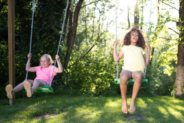 istock Two happy girls swinging in sunny backyard, front view 1440641135