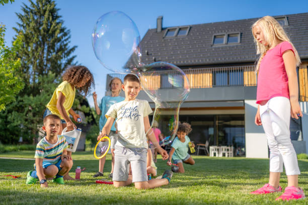 istock Kids blowing huge soap bubbles outdoors, sitting on grass 1440641146