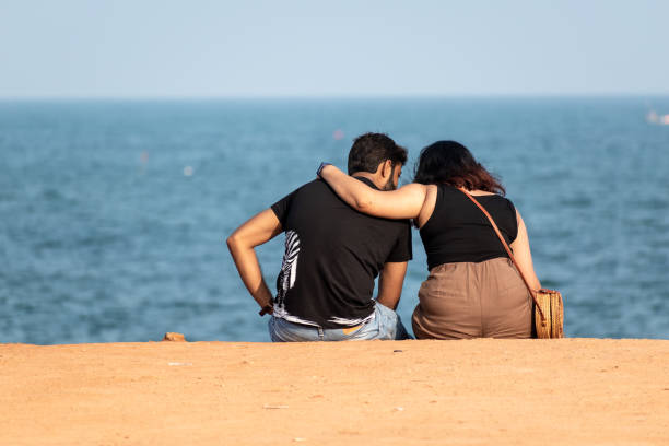 Pondicherry, India - January 2020: Back shot of a romantic Indian couple sitting by the seaside promenade.