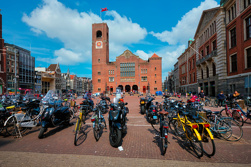 Amsterdam, Netherlands - May 7, 2017: Beursplein with parked bicycles motorcycles and Beurs van Berlage building former commodity exchange building now venue for concerts, exhibitions and conferences
