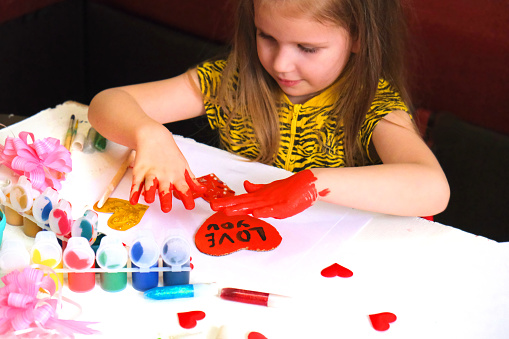 Child making homemade greeting card. A little girl paints a hearts as a gift for Mothers Day or VAlentines day. Traditional play concept. Arts and crafts concept.