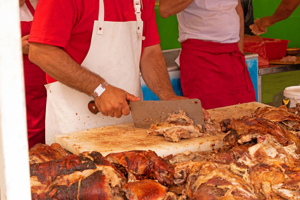 Man using clever to cut  roasted meat and selling it on local fair stall