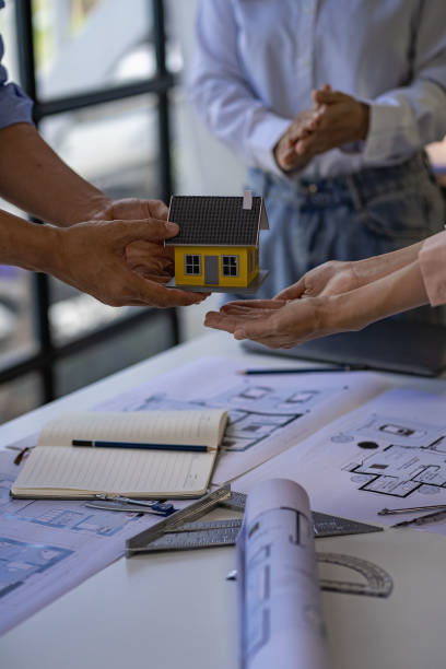 istock Architects and engineers point to buildings on blueprints and use laptops to draw house project designs in a construction concept office. 1440659196