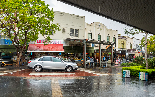 Sydney, Australia - Oct 2, 2021: Car driving through a narrow road with pedestrian crossing in blurred motion, under heavy rain. Opposite are many Asian stores. Busy commercial area.