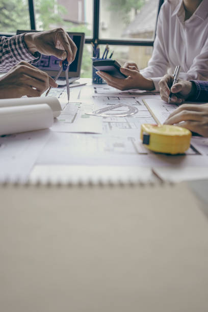 istock Architects and engineers point to buildings on blueprints and use laptops to draw house project designs in a construction concept office. 1440659270