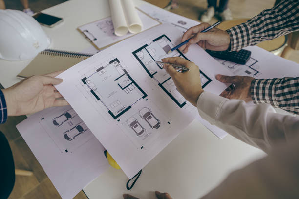istock Architects and engineers point to buildings on blueprints and use laptops to draw house project designs in a construction concept office. 1440659290