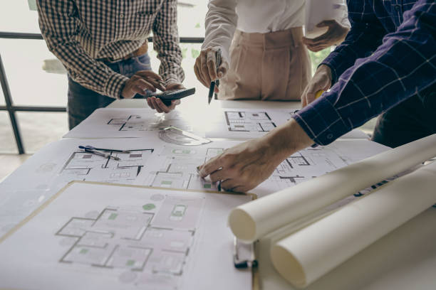 istock Architects and engineers point to buildings on blueprints and use laptops to draw house project designs in a construction concept office. 1440659291